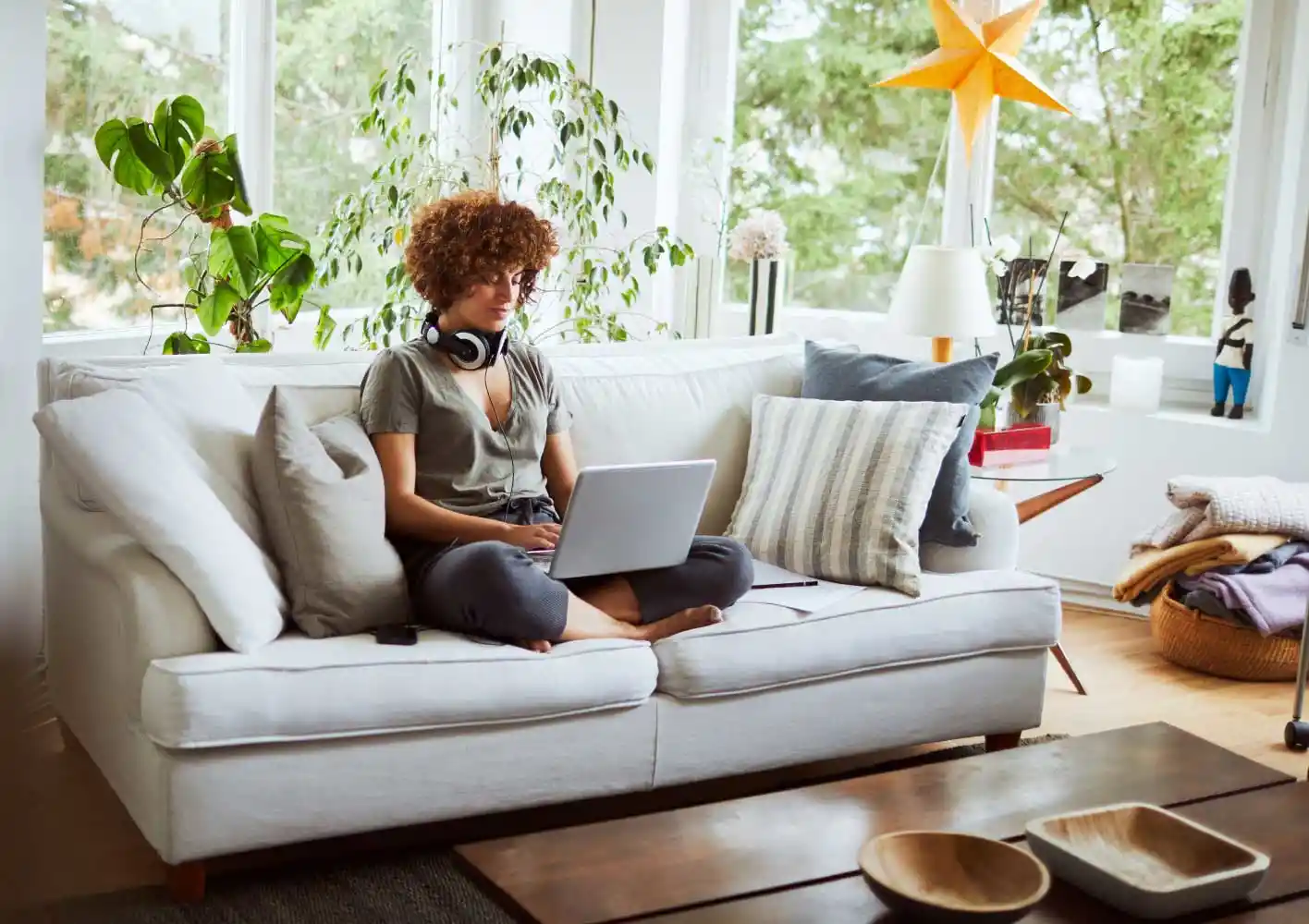 Uma mulher trabalhando em home office, sentada no sofá com um notebook no colo