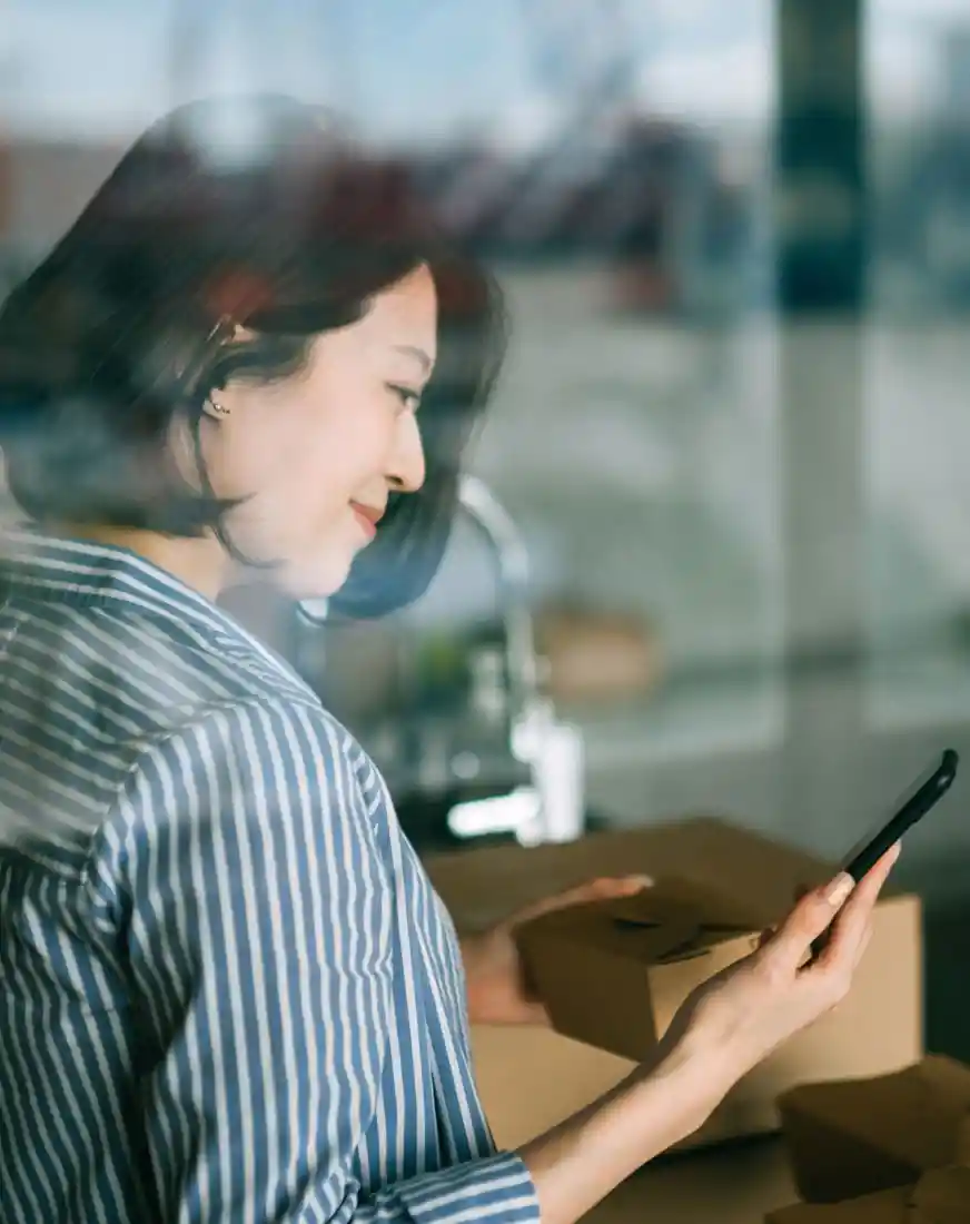 Smiling woman standing by the kitchen counter, ordering food using smartphone.