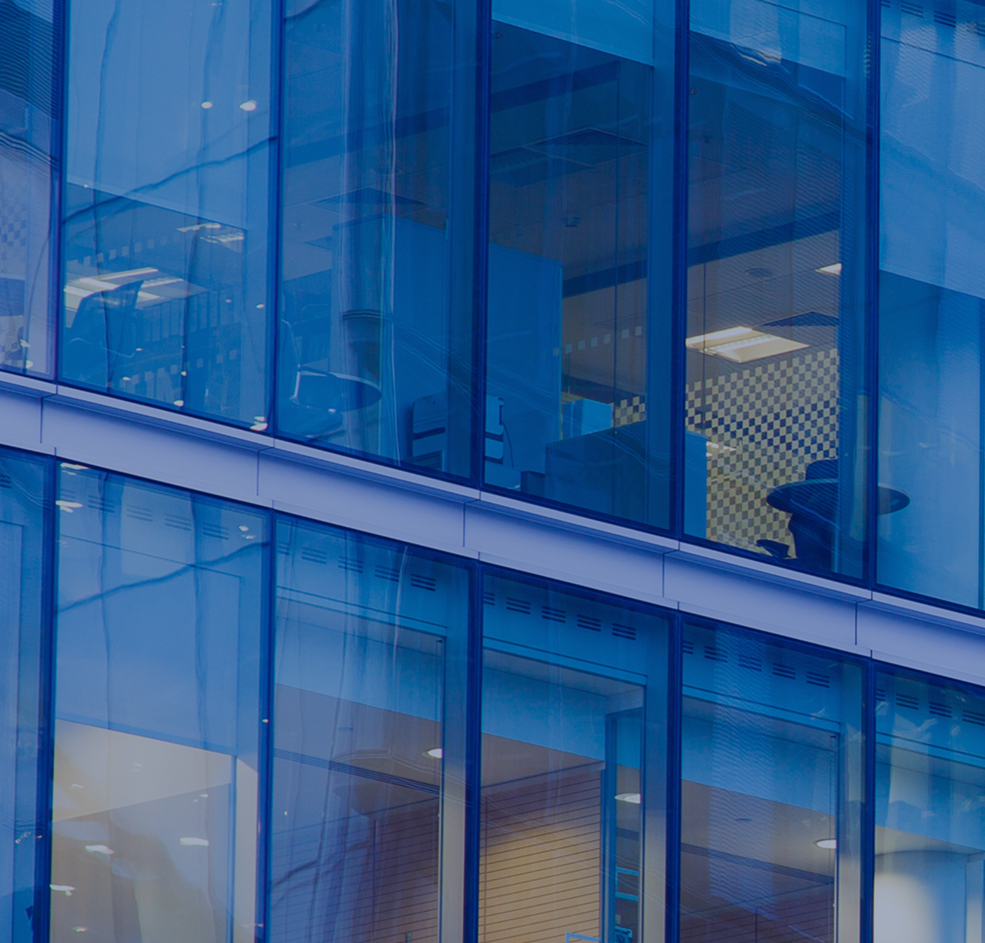 A tall glass office building with views into employees' work stations.